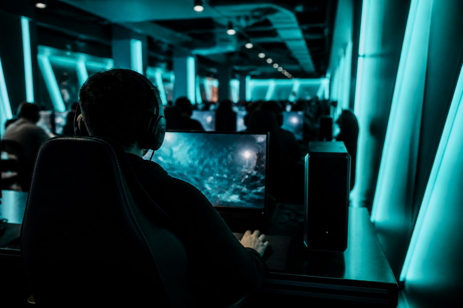 A player in headphones leaning in and concentrating at a lit gaming station
